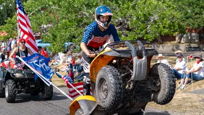 A rider pops a wheelie on an ATV decorated with American flags during the Fourth of July parade in Home, Washington.